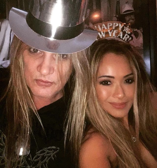 Sebastian in a silver hat and black t-shirt posing with his wife.